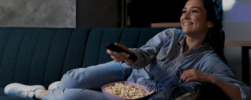 Pessoa assistindo TV e comendo pipoca confortável no sofá